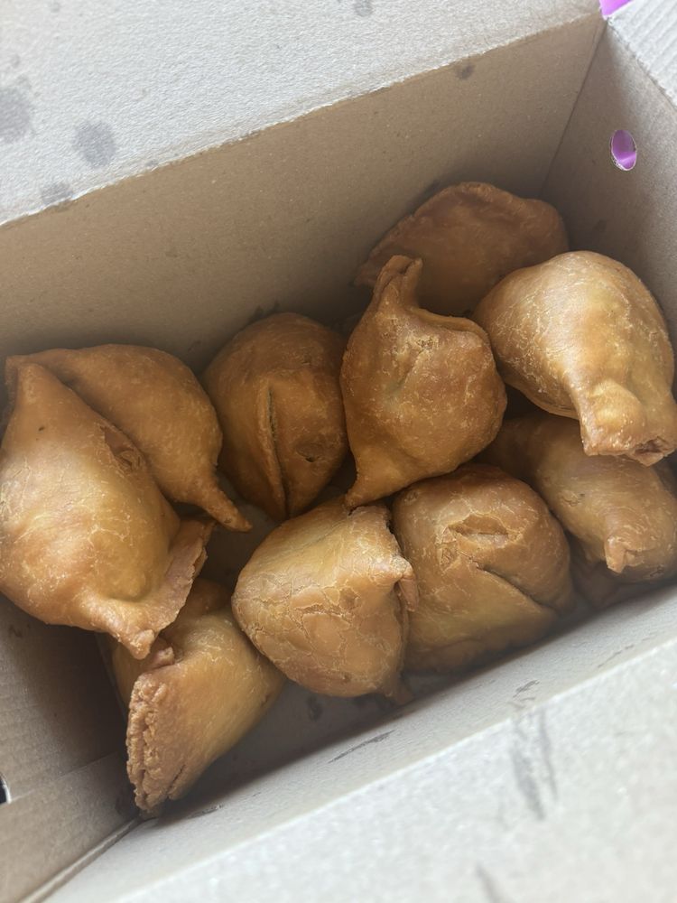 Golden brown crispy samosas piled up in a display container.
