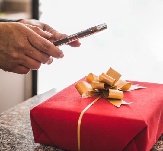 Person hands tying a yellow ribbon around a red gift box.
